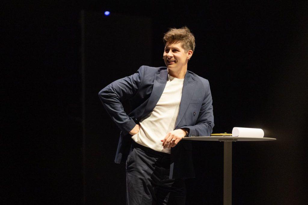 Keynote speaker Ben Hanlin on stage with his notes on the table beside him