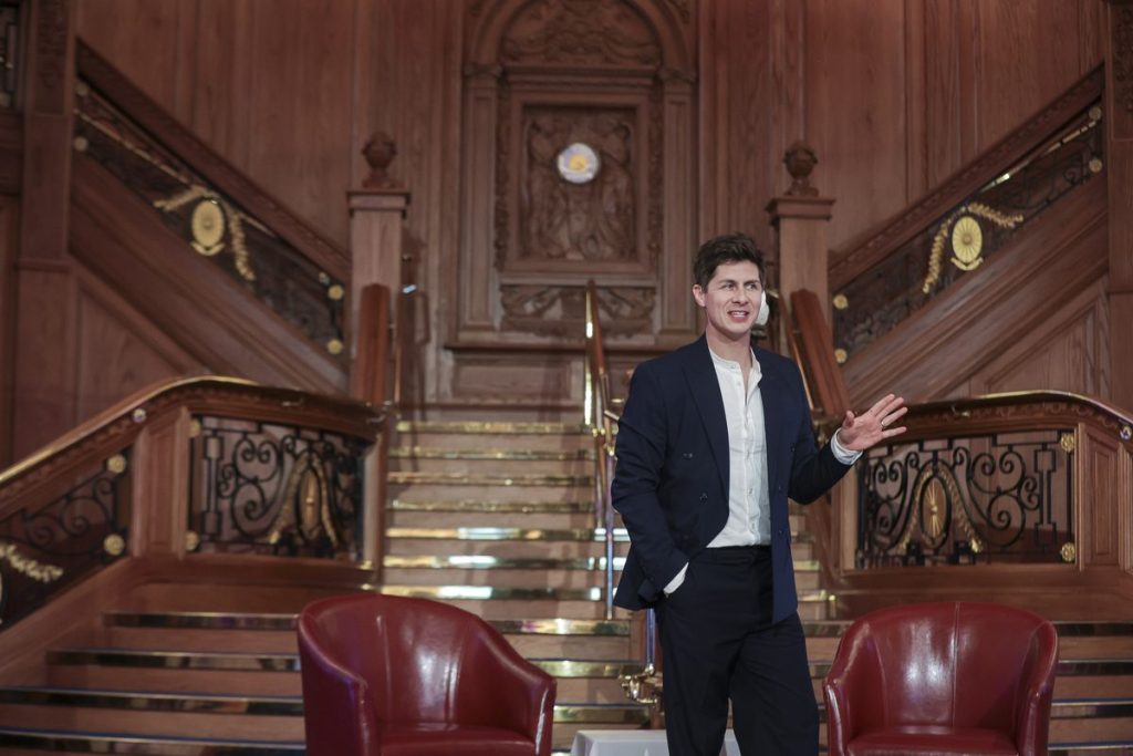 Ben Hanlin speaking to an audience in front of a grand staircase at a corporate event